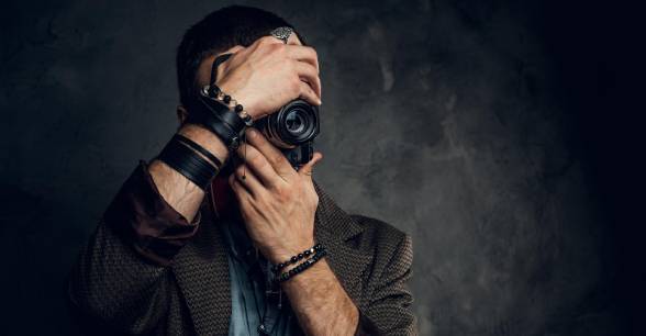 Person taking a photo with a vintage camera against a dark, textured background.